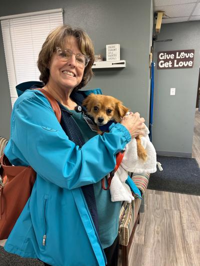 Smiling person holding a small brown puppy