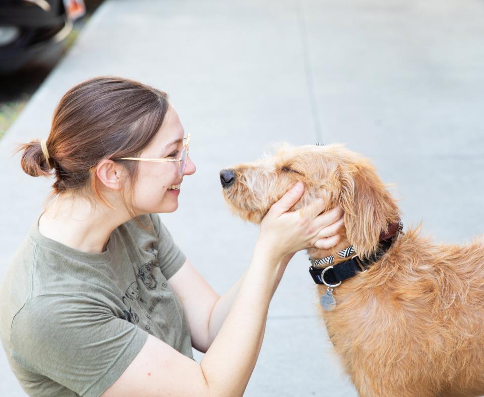 Profile of smiling person who is affectionately holding the head of a tan dog