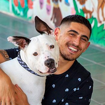 Smiling person hugging a happy dog with colorful wall behind them