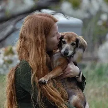 Person standing outside under a tree while holding a small dog close to them